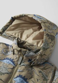 Veste à capuche avec un motif de dinosaure en tissu beige, ornée d'illustrations bleues, vertes et grises, et dotée d'une fermeture à glissière centrale.