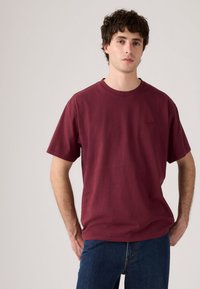 Burgunderfarbenes Baumwoll-T-Shirt mit Rundhalsausschnitt und kurzen Ärmeln, ausgestattet mit einem dezenten Logo in der gleichen Farbe auf der Brust.