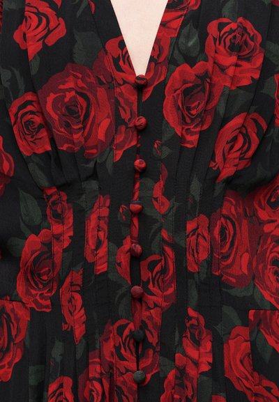 Μαύρο φόρεμα από ύφασμα με τύπωμα κόκκινου τριαντάφυλλου, V-λαιμόκοψη και κουμπιά στο μπροστινό μέρος σε αντίστοιχη απόχρωση, με πιέτες που προσθέτουν υφή και δομή.