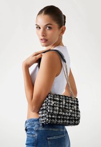 Borsa a tracolla in tweed bianco e nero con una texture trapuntata, dotata di una tracolla in catena argentata e un dettaglio in pelle nera. Contiene il dettaglio del logo.