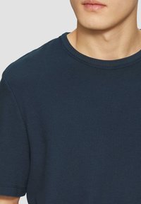 Granatowa koszulka z krótkim rękawem, wykonana z teksturowanej tkaniny, z klasycznym okrągłym dekoltem i przeszytymi detalami u dołu.