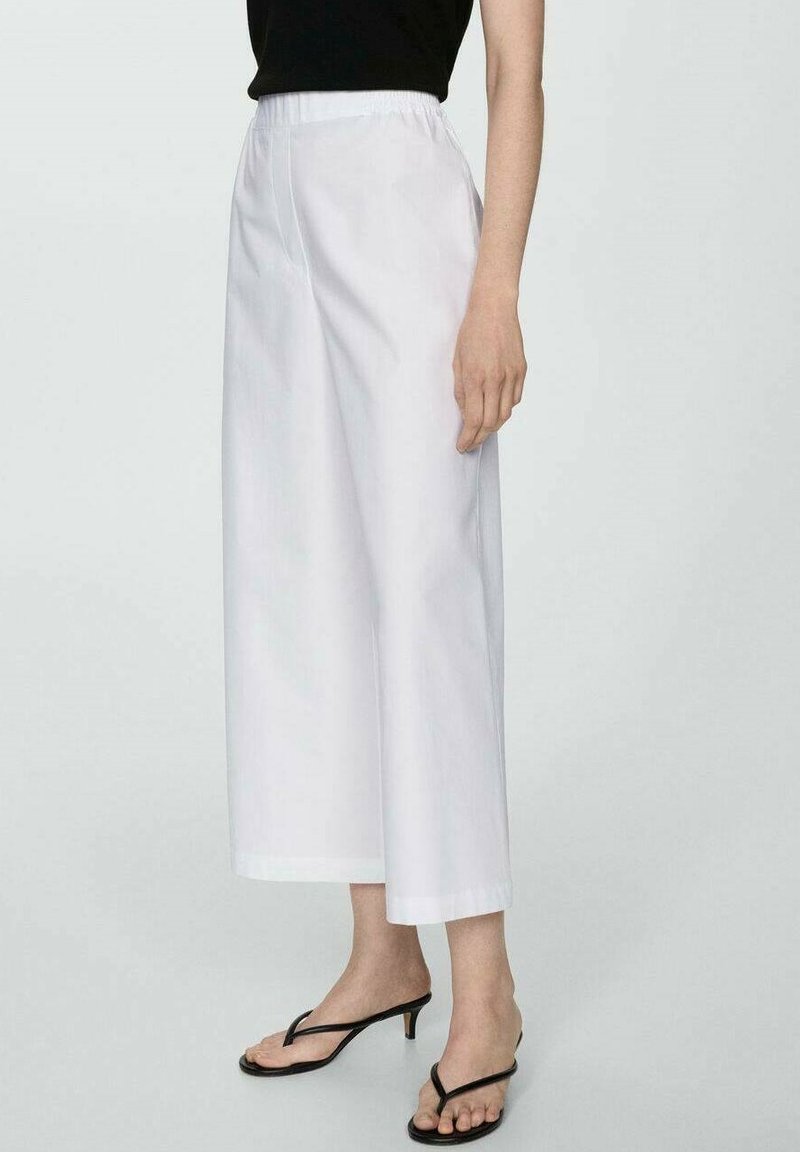 Witte, wijde broek met elastische tailleband, met een gladde textuur en een verkorte lengte. Samen met zwarte sandalen.