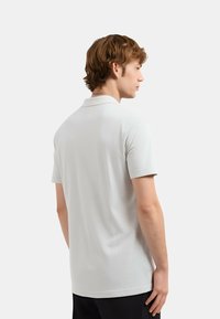 Polo di colore grigio chiaro con una texture morbida, dotato di colletto classico e maniche corte. La parte posteriore è semplice con cuciture sottili.