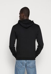 Sudadera negra con capucha ajustable, corte entallado, hecha de una tela suave. Presenta un dobladillo y puños acanalados, combinada con jeans de color azul claro.