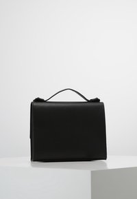 Černá kožená kabelka s pevnou konstrukcí, obdélníkového tvaru, s horní rukojetí a jemnou texturou. Vyznačuje se minimalistickým vzhledem bez viditelných ozdob.
