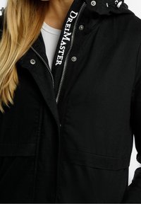 Černá bunda se zipem vpředu, patentkami a dvěma předními kapsami. Obsahuje kapuci na šňůrku a logo na límci.