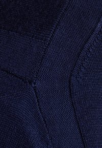 Granatowa dzianina o różnych fakturach i splotach; zawiera gładkie sekcje oraz podniesione szwy; zbliżenie na detale materiału.