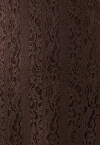 Tessuto in pizzo marrone con motivi floreali e righe orizzontali. La texture è intricata e delicata, mostrando una qualità traslucida.