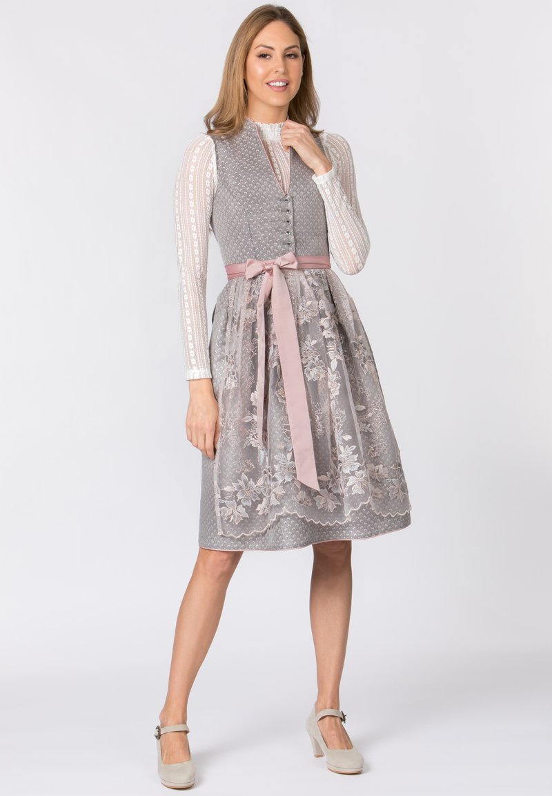 Graues traditionelles Kleid mit floralem Spitzenoverlay, rosa Satinband in der Taille und weißer strukturiertem Bluse mit langen Ärmeln und Knopfverschluss.