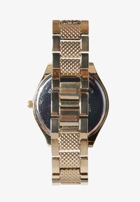 Montre en or avec un bracelet en maille métallique et un cadran rond réfléchissant. Les maillons détaillés alternent avec des sections texturées dans le bracelet.