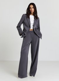 Completo giacca e pantaloni su misura grigio, con un delicato motivo di piccoli puntini bianchi, dalla texture liscia e dal taglio a gamba larga.