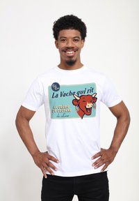 Vit bomull t-shirt med grafiken "La Vache qui rit" som visar en leende ko, vintage-stil, blå bakgrund och färgglada textaccenter.