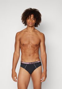 Schwarze Sloggi-Unterhosen mit einem kontrastierenden elastischen Bund, der mehrfarbige Streifen aufweist. Glattes Material, niedriger Schnitt und keine sichtbaren Muster.
