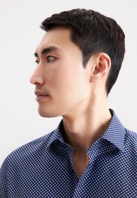 Navyblauwe shirt met witte stippen, met een knoopsluiting aan de kraag en korte mouwen. Glad materiaal met een subtiele glans.