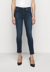 Mörkblå skinny jeans i denim, med medelhög midja, fem fickor och fransat nederkant. I kombination med svarta högklackade skor.