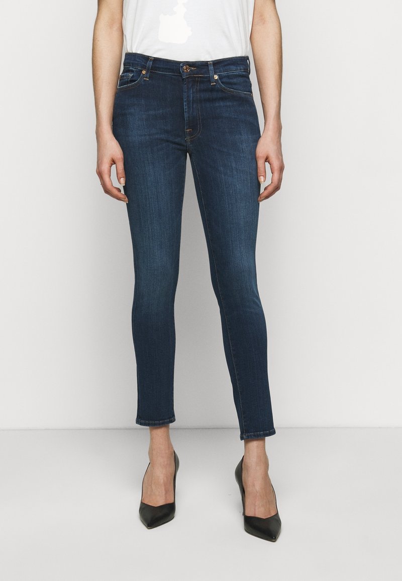 Mörkblå skinny jeans i denim, med medelhög midja, fem fickor och fransat nederkant. I kombination med svarta högklackade skor.