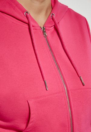Rózsaszín, smooth anyagból készült, cipzáros kapucnis pulcsi elülső zsebbel, ezüst cipzárral és fém véggel ellátott húzózsinórokkal.