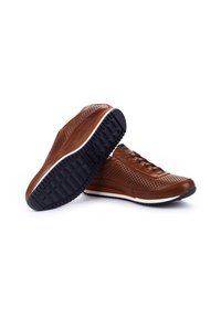 Sneaker in pelle marrone con tomaia perforata, suola intermedia bianca e suola esterna in gomma nera robusta con un motivo di battistrada testurizzato.