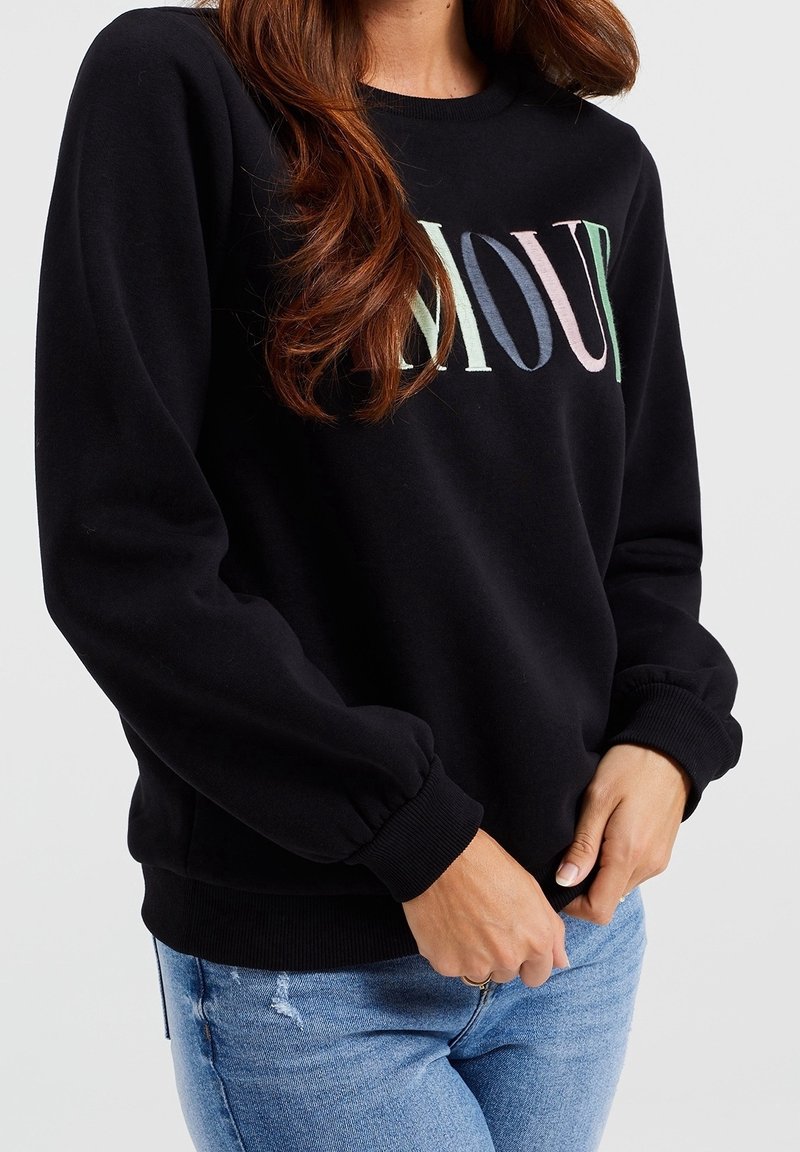 Svart sweatshirts med långa ärmar, ribbade ärmslut och rund halsringning. Har "AMOUR" tryckt i flerfärgade bokstäver på framsidan.