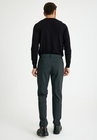 Dunkelgraue Herrenhose im Slim-Fit mit strukturiertem Stoff, mit Gesäßtaschen, kombiniert mit einem schwarzen Langarmhemd und schwarzen Sneakers.