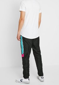 Sorte træningsbukser med sidepaneler i teal og lyserød, med elastisk talje og tapered ben. Kombineret med hvide sneakers.