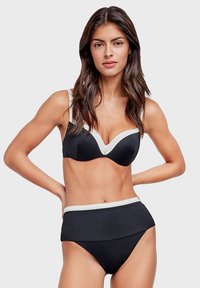 Bikini nero con un top balconcino strutturato e modellato, decorato con accenti bianchi. Parte inferiore a vita alta con tessuto nero solidale e texture liscia.