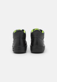 Baskets hautes en cuir noir avec une finition texturée, des accents verts sur le col et une semelle en caoutchouc noire avec des détails de ventilation.