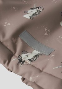 Stoff med unicorn-mönster, mjuk rosa bakgrund, med en grå etikett. Designen inkluderar fantasifulla mönster av unicorn och hjärtan.