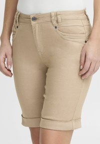 Pantalones cortos de mezclilla en tono tostado con un diseño ajustado, dobladillos enrollados y bolsillos frontales. Presentan un cierre de botón y detalles de costura sutiles.