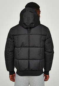 Schwarze Pufferjacke mit Kapuze, mit gesteppten Einsätzen, elastischen Bündchen und einstellbarem Rückengurt. Glatte Textur.