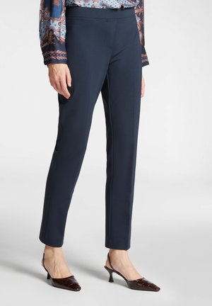 Marinblå skräddarsydda byxor med en jämn textur och slim fit, utrustade med ett stretchigt midjeband. Matchas med bruna, vadderade klackskor med spetsig tå.