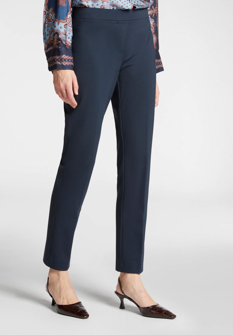 Meriputih yang dirancang khusus dengan tekstur halus dan potongan ramping, dilengkapi dengan pinggang elastis. Dipadukan dengan sepatu hak tinggi berbentuk runcing berwarna cokelat yang berlapis.