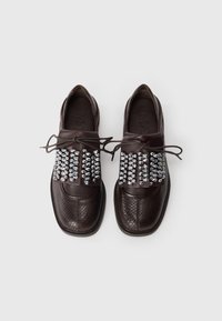 Dark brown leather loafers with textured pattern and metallic silver studs across the top, tied with thin brown laces on a white background.