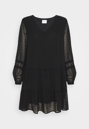 Robe noire à manches longues avec encolure en V, manches transparentes texturées, jupe à étages et petit motif en forme de cœur sur tout le tissu.