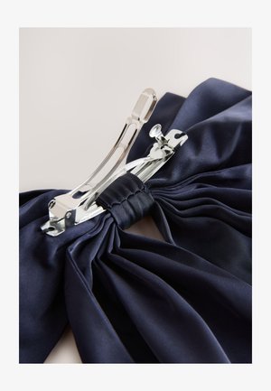 Tumesinine satiinriie, millel on voltimised, kinnitatud keskel stiilse hõbedase metallkliibiga, millel on sujuvad servad ja poleeritud viimistlus.