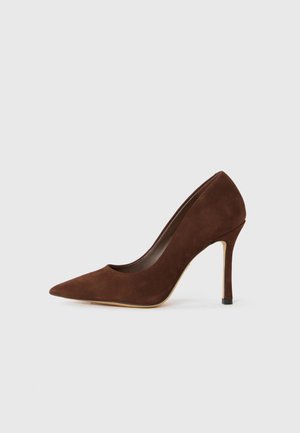 Pump con punta a scarpa in suede marrone, tacco a stiletto sottile, mostrato su uno sfondo bianco.