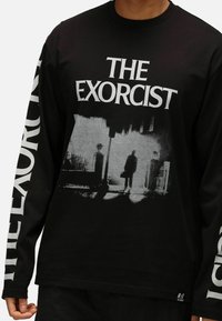 Långärmad svart t-shirt i bomull med en gråskalig grafik från "The Exorcist" på framsidan och fet vit text längs ärmarna.
