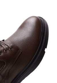 Bota de cuero marrón con un acabado texturizado, puntera redonda y suela de goma negra. Cuenta con ojetes metálicos y cordones para un ajuste seguro.