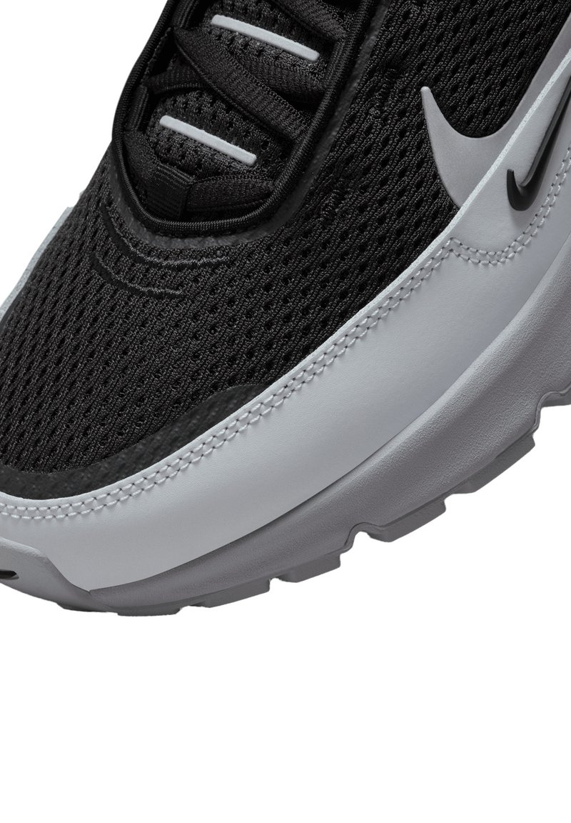 Scarpa con tomaia in mesh nero e suola in gomma grigia, con il logo Nike bianco, lacci neri e dettagli testurizzati lungo il bordo.