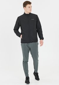 Svart lättviktsjacka med hög krage, dragkedjestängning och logotyp. Matchas med grå tapered-byxor med svarta sidostrecker och svarta sneakers.