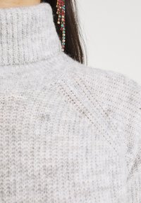 Light gray knitted turtleneck sweater with a textured pattern and ribbed collar, featuring finely woven yarn for added warmth.