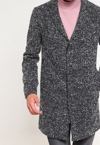 Black and white speckled wool coat with a notched collar, front button closure, and long sleeves. Textured fabric, knee-length design.