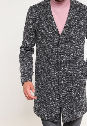 Cappotto in lana maculato bianco e nero con colletto a punta, chiusura con bottoni frontali e maniche lunghe. Tessuto testurizzato, design fino al ginocchio.