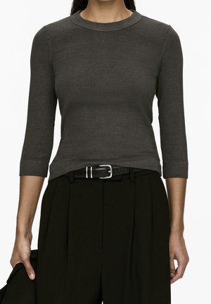 Personne portant un haut côtelé gris foncé ajusté avec des manches trois-quarts, rentré dans un pantalon noir taille haute avec une ceinture noire.