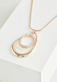 Ogrlica s privjeskom od ružičastog zlata s preklapajućim oblicima suze, od kojih jedan sadrži prozirne rhinestone, na glatkom metalnom lancu.