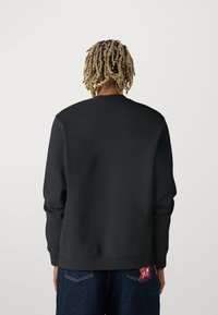 Sudadera negra con cuello redondo y mangas largas, hecha de una tela suave. La parte trasera presenta un diseño minimalista con un acabado texturizado.