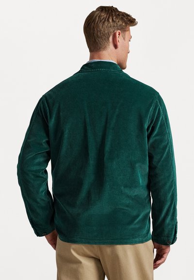 Green corduroy jacket with long sleeves, a collar, and visible texture lines. Features buttoned cuffs and a tailored fit.