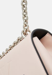 Bolso sintético de color rosa claro con una correa de cadena plateada y un borde negro en contraste. Presenta un detalle de logo en relieve y una superficie de textura suave.