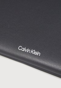 Puzdro na zápisník Calvin Klein v námorníckej textúrovanéj látke s bielym embosovaným logom. Jednoduchý, elegantný dizajn s hladkým povrchom.