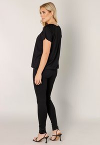 Zwarte top met korte mouwen en een ontspannen pasvorm, gecombineerd met zwarte leggings en hakken. Gladde stof, eenvoudig ontwerp en zijsplitjes aan de zoom.